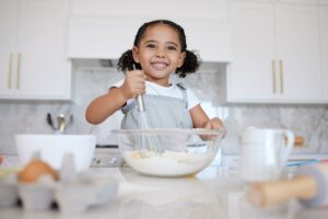 A imagem mostra uma menina sorridente na cozinha.