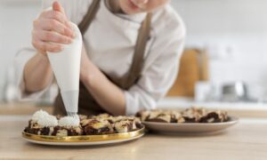 Cozinheira finalizando doces com chantilly em bandeja, preparados com insumos do Vantajão Atacado.