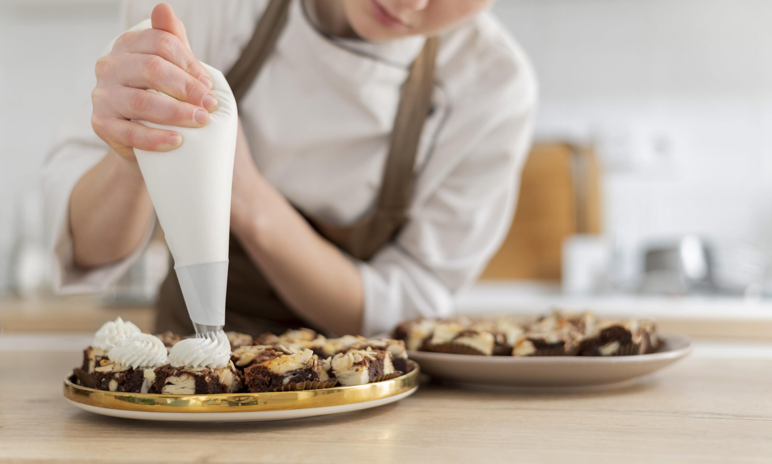 Cozinheira finalizando doces com chantilly em bandeja, preparados com insumos do Vantajão Atacado.