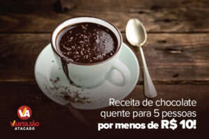 Na imagem é possível ver uma xícara branca cheia de chocolate quente. A bebida tem raspas de chocolate em cima e escorre pela borda da xícara. No pires está um pedaço de chocolate.