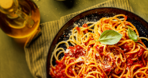 prato preto colocado acima de um pano, com espaguete, molho vermelho e queijo ralado com folhas de manjericão de complemento, e um recipiente com azeite de oliva ao lado