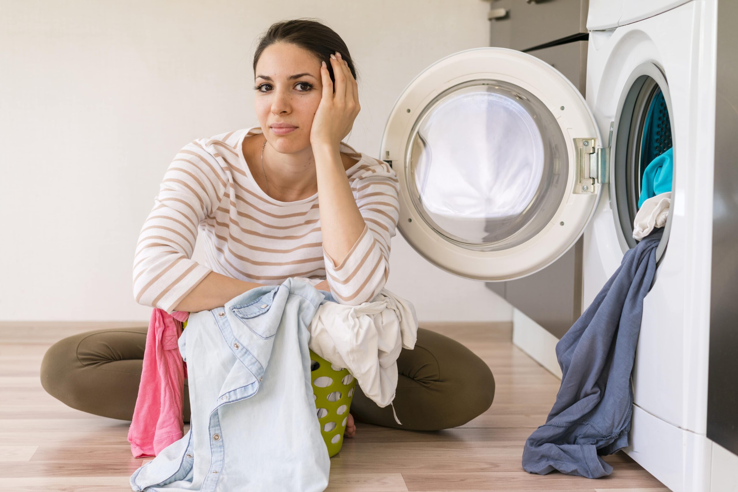 A imagem mostra uma pessoa sentada em frente à máquina de lavar roupas.