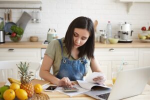 A imagem mostra uma mulher calculando em uma cozinha.
